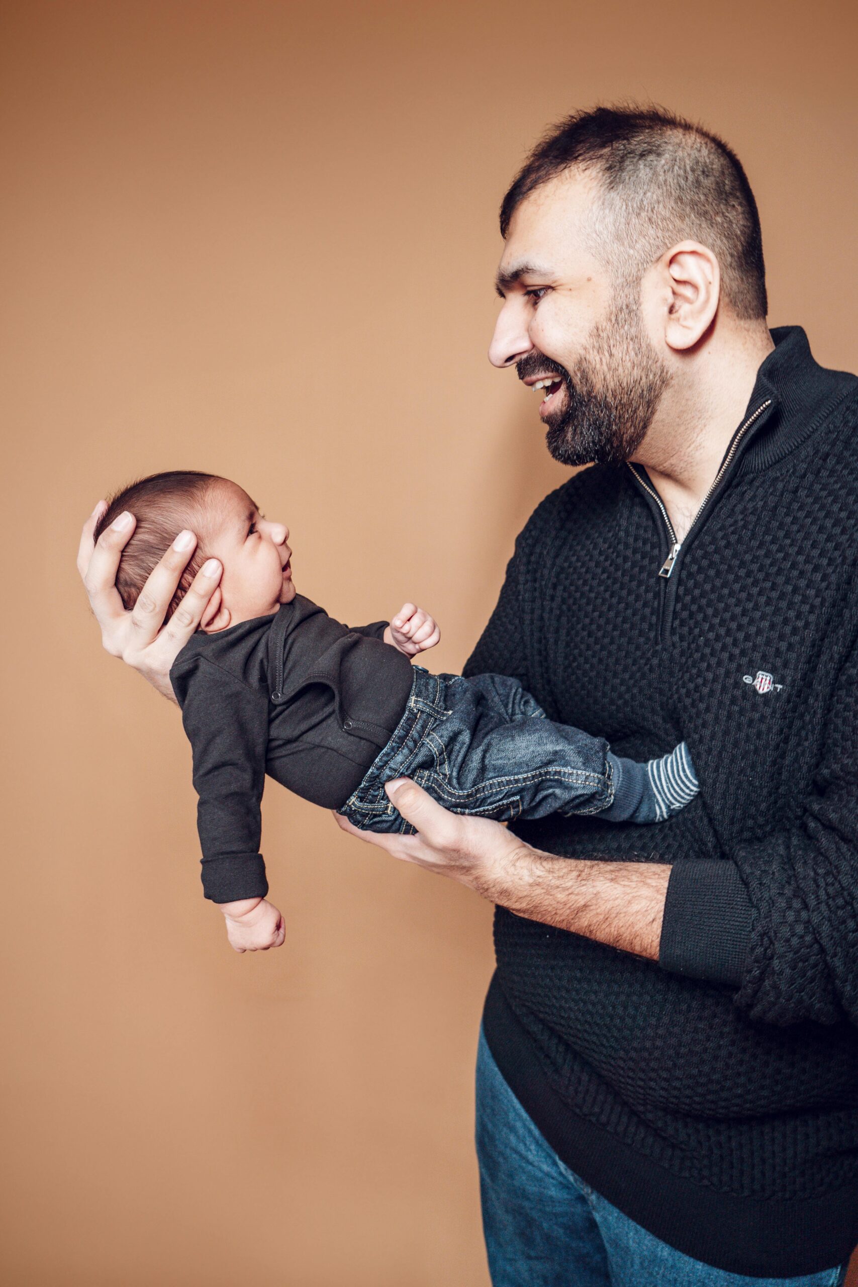 A father joyfully holding his baby against a brown backdrop, showcasing love and parenting.